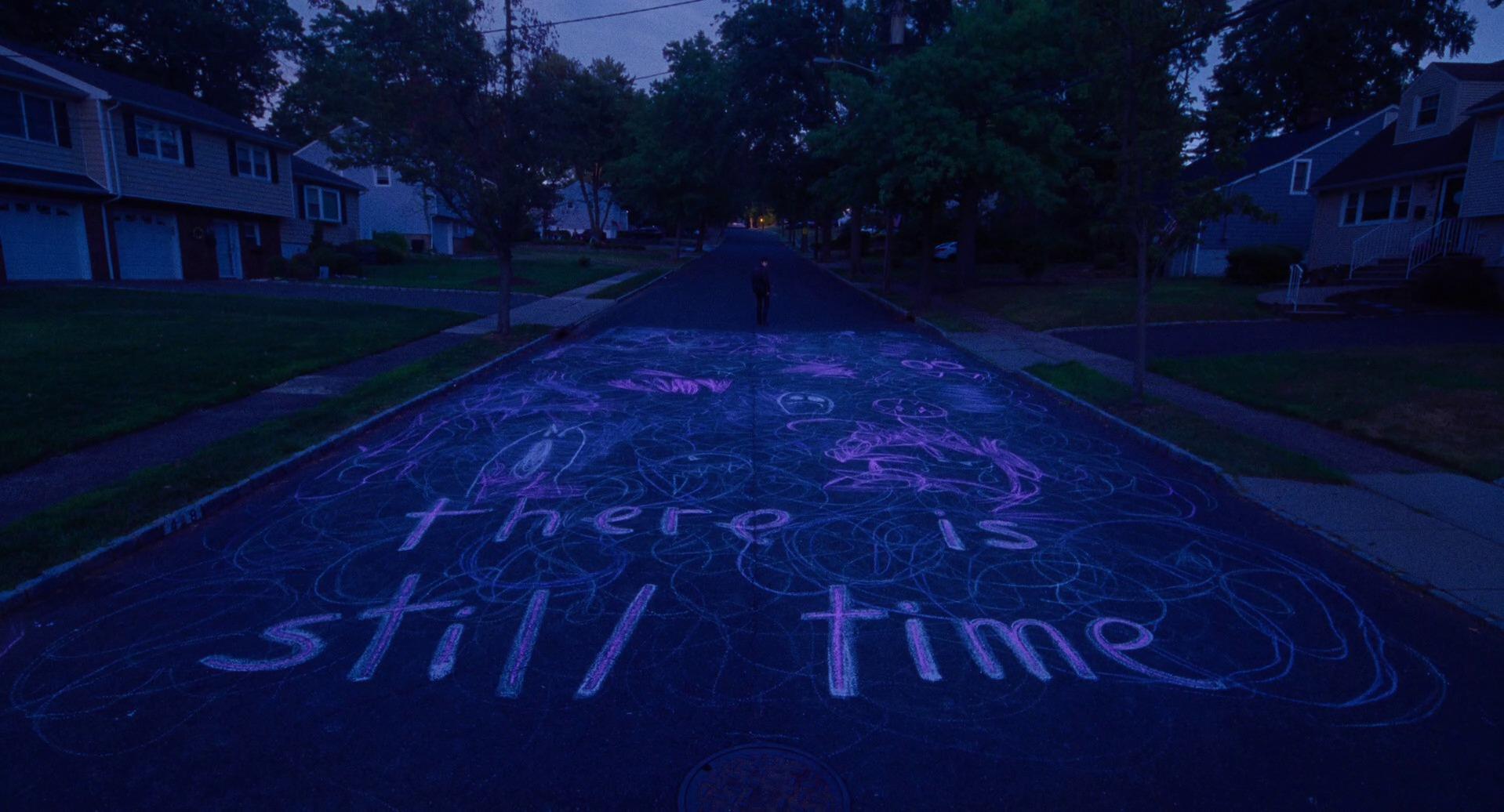 chalk drawings on a darkening suburban street, with the words 'there is still time' written on the ground